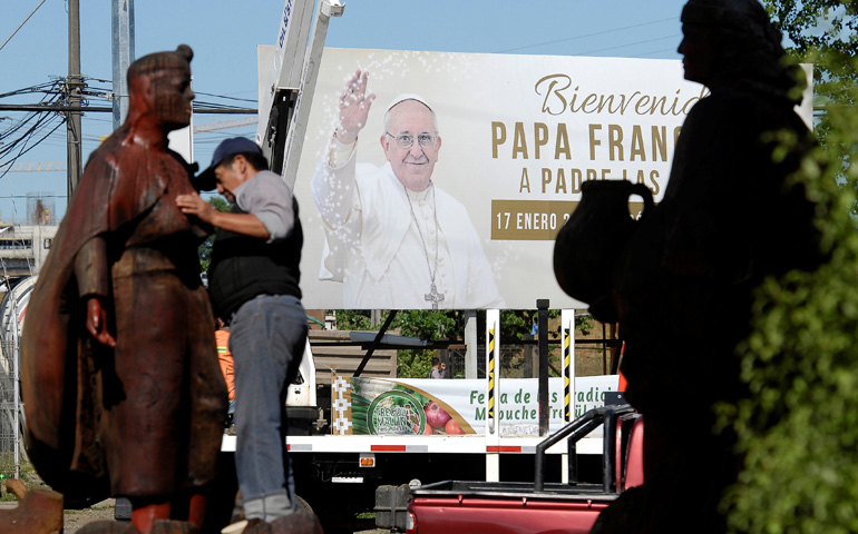 Un hombre limpia una escultura mapuche frente a un cartel que anuncia el viaje del Papa Francisco a Chile, en Temuco, el 10 de enero de 2018