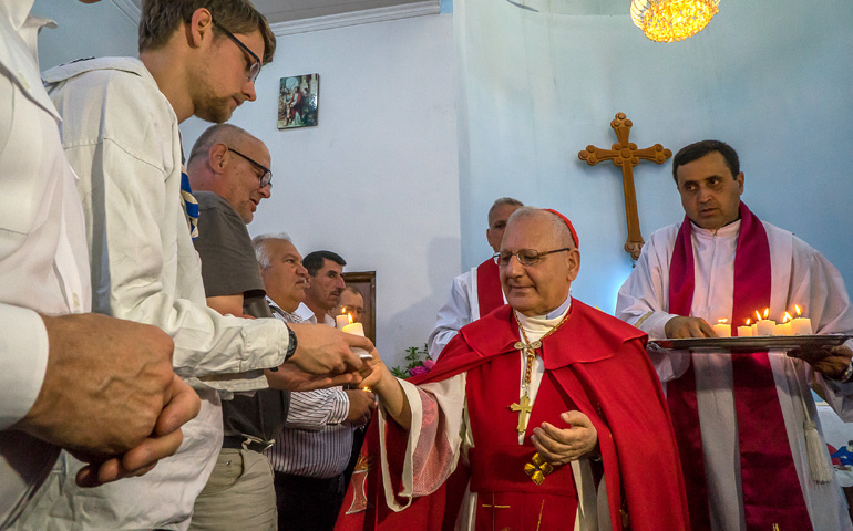 El patriarca Sako reparte unas velas entre los fieles que participan en la celebración del Jueves Santo, en abril de 2017, en la iglesia de San Esteban en Malabarwane.