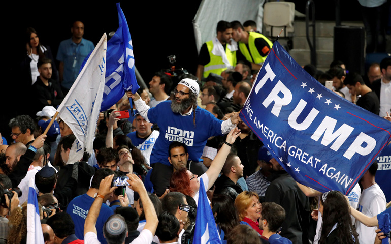 Un partidario de Benjamín Netanyahu celebra su victoria ondeando una bandera de apoyo al presidente estadounidense Donald Trump
