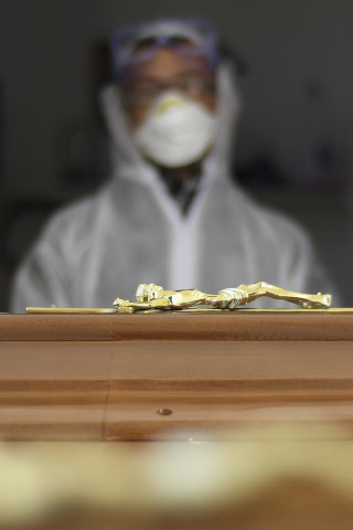 Empleado de los servicios funerarios ante el féretro de una víctima del COVID-19