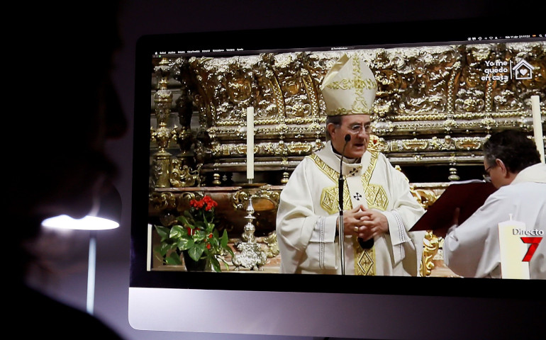 Una persona participa a través de la televisión de la Vigilia Pascual, presidida por monseñor Juan José Asenjo, en la catedral de Sevilla