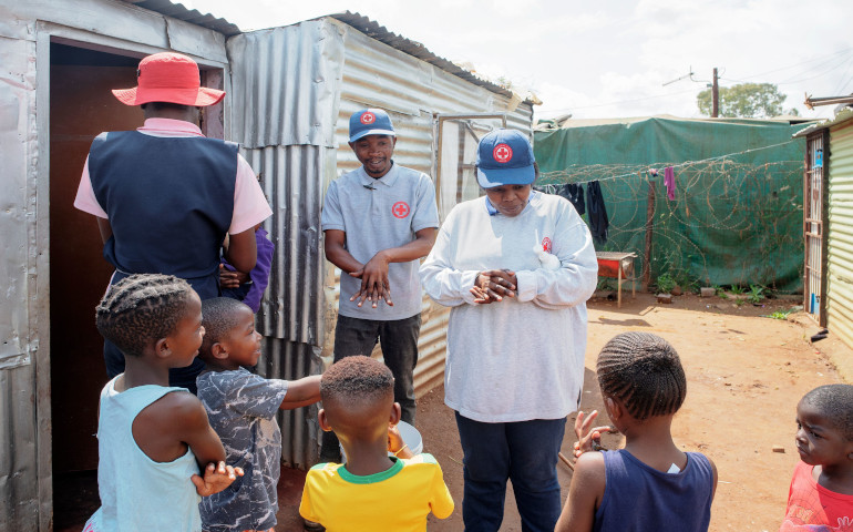 Un miembro de Cruz Roja Internacional enseña a unos niños a lavarse las manos para tratar de contener el COVID-19, en un asentamiento de Soweto (Sudáfrica)