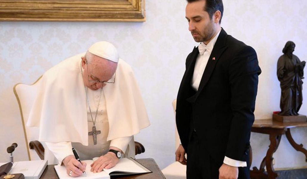 Francisco firma en el libro que ha regalado al embajador turco