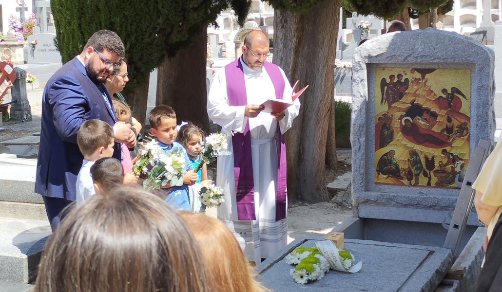 Familia con niños pequeños en un cementerio, con un sacerdote
