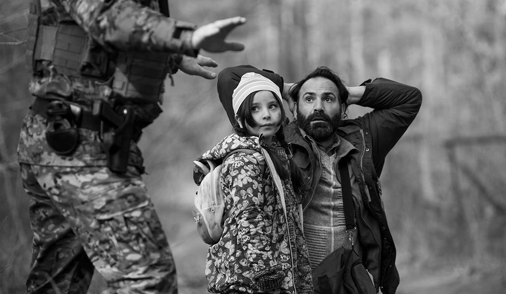 Un padre y su hija migrantes frente a un guardia de frontera