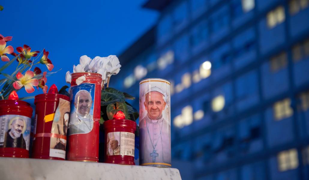 Velas y flores en la base de la estatua de san Juan Pablo II en el exterior del hospital Gemelli de Roma, donde el Papa Francisco está recibiendo tratamiento debido a una neumonía doble
