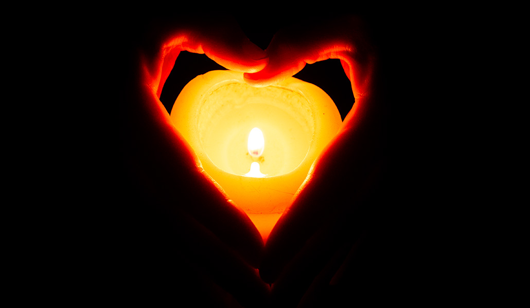 Imagen de recurso de una vela encendida entre unas manos que forman un corazón