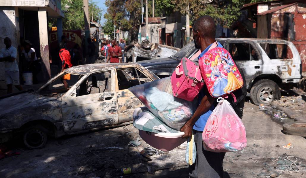 Un hombre carga sus pertenencias y observa los coches quemados en un barrio de Puerto Príncipe