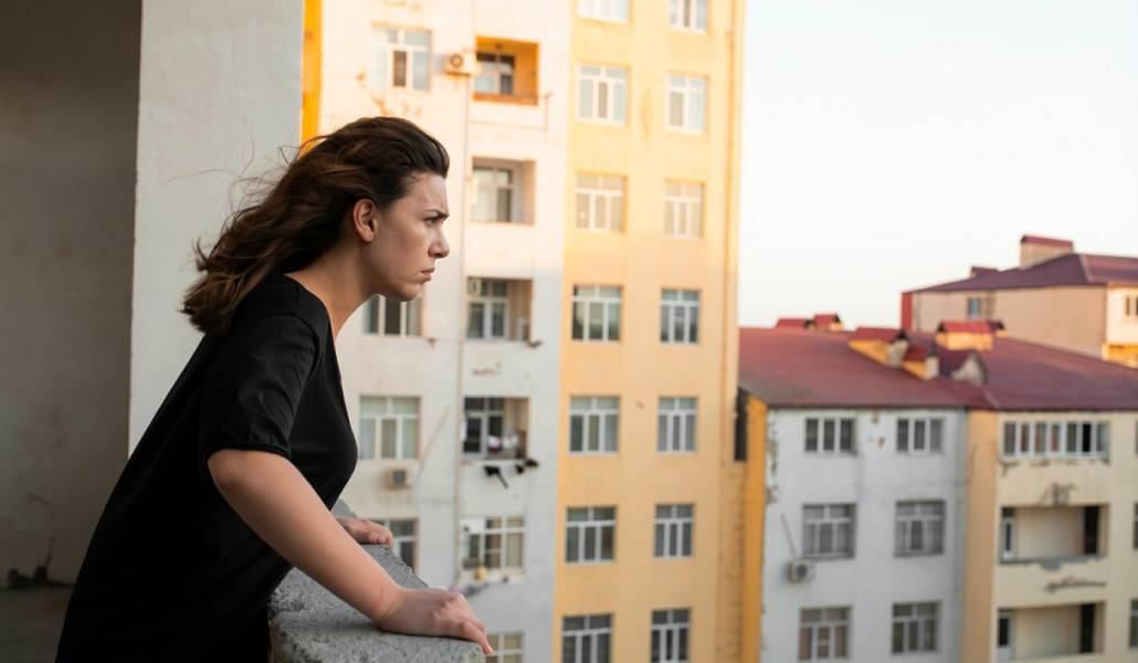 Imagen editada con IA de una mujer mirando seria bloques de viviendas desde su terraza.